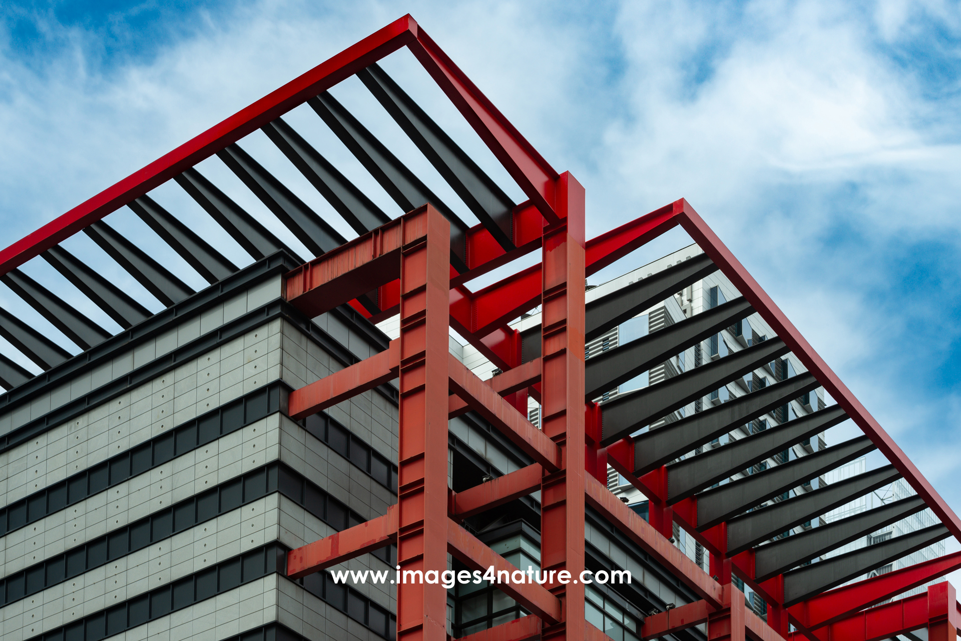 Low-angle view of shopping center with modern red and black metal design against blue sky
