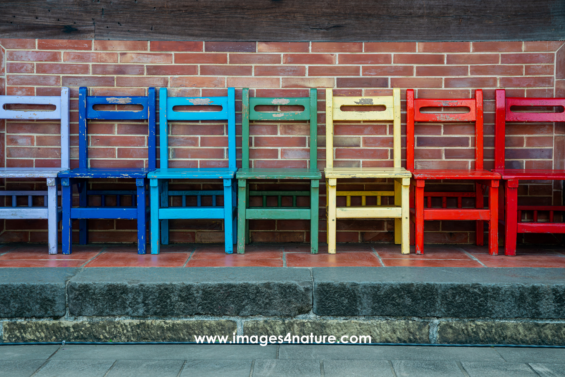 Line-up of seven weathered wooden chairs, each painted in a different color, making them look like a rainbow