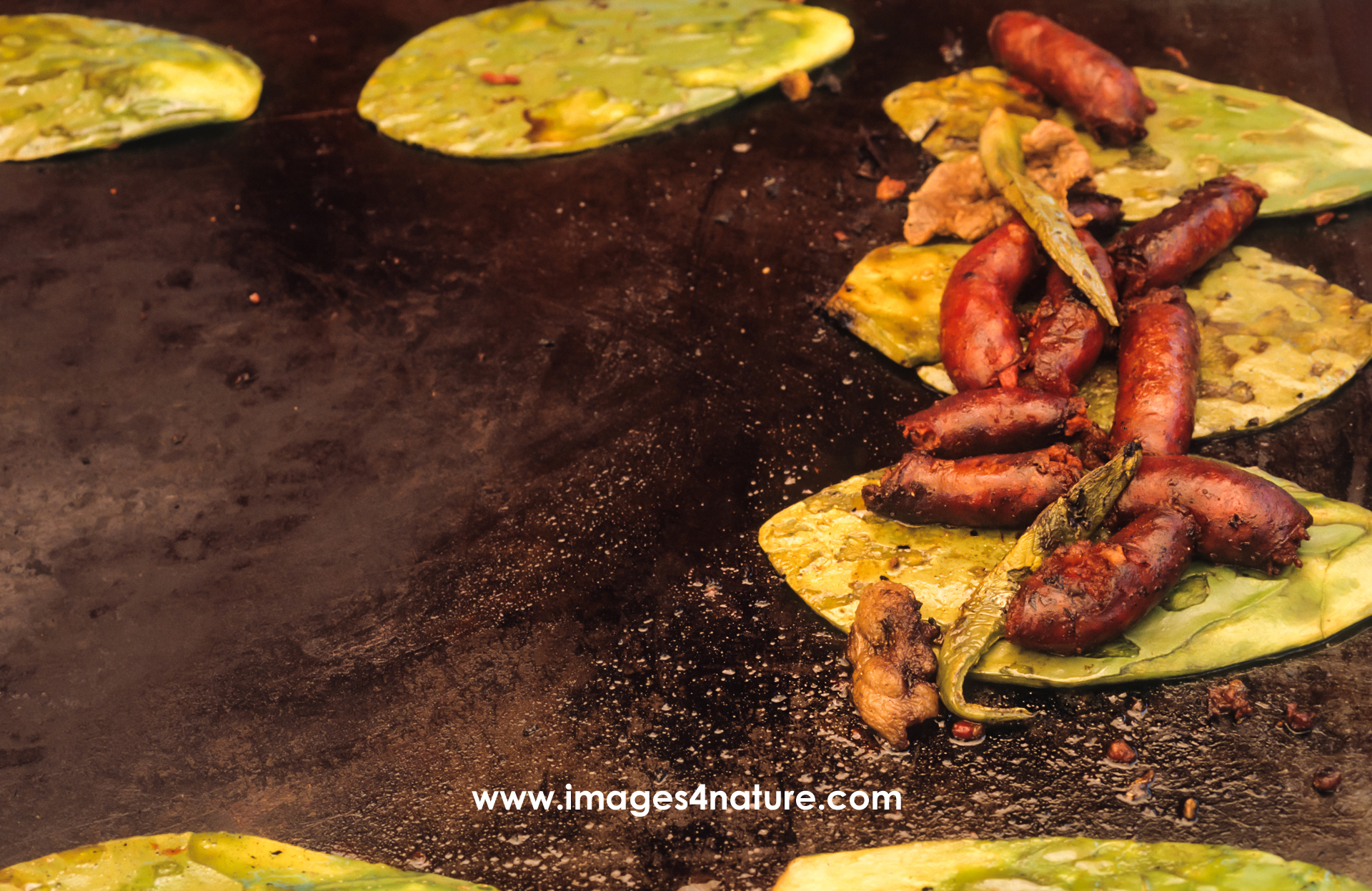 Cactus pads being grilled on a hot metal surface with some chorizo sausage on top