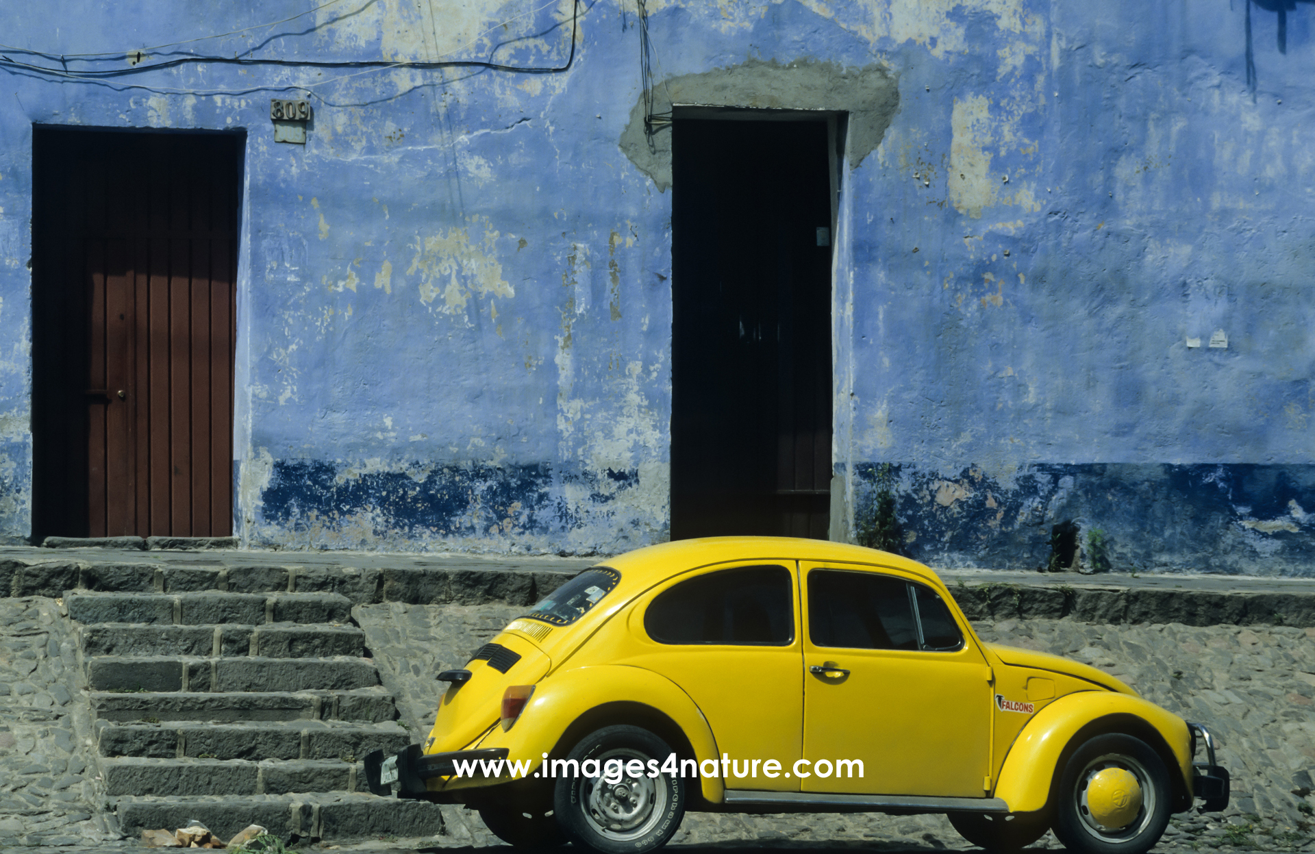 A yellow Volkswagen Beetle parked in front of an old building with blue walls