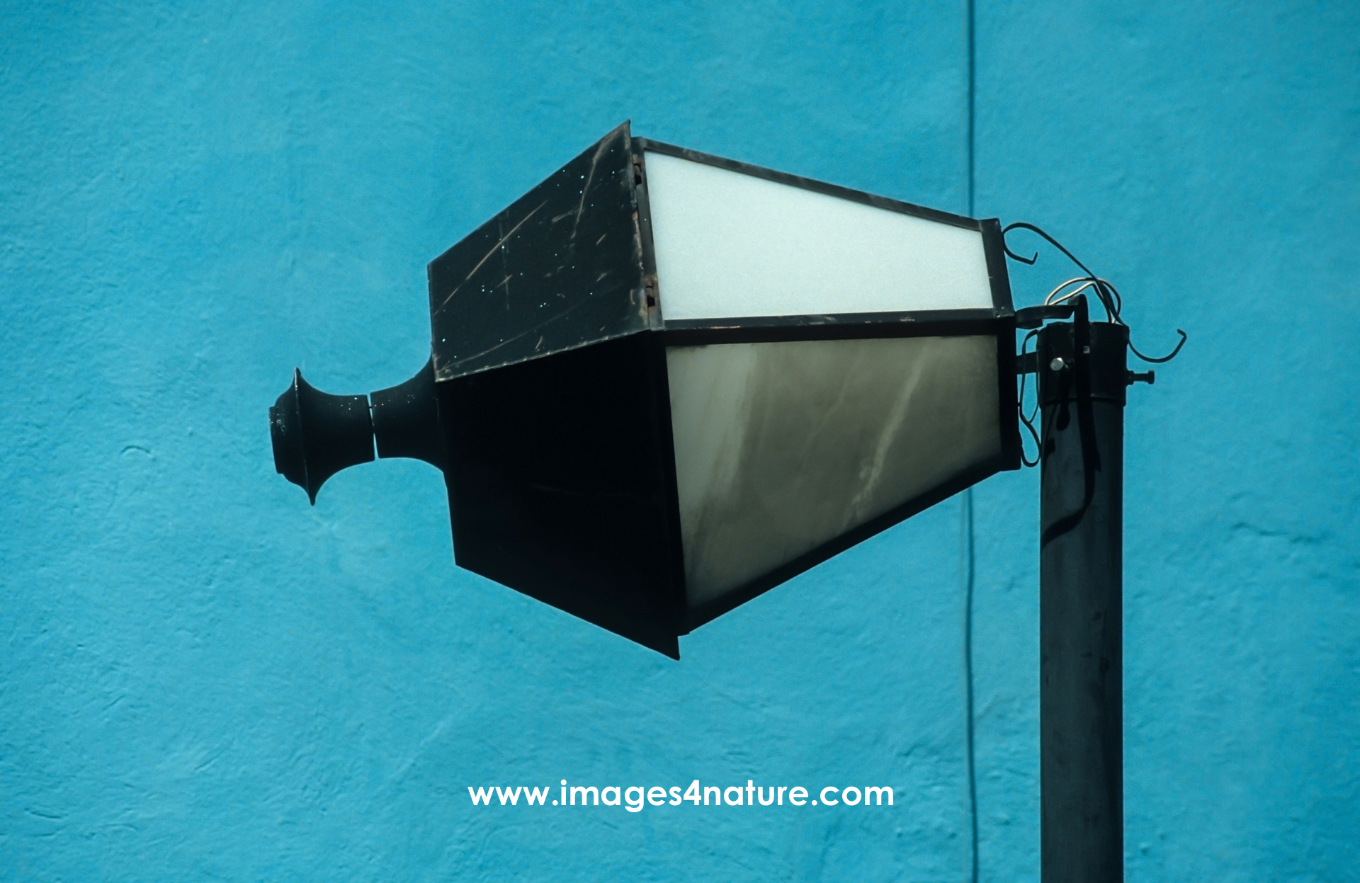 Close-up of a black metal street lantern with its shade bent off in a 90 degrees angle