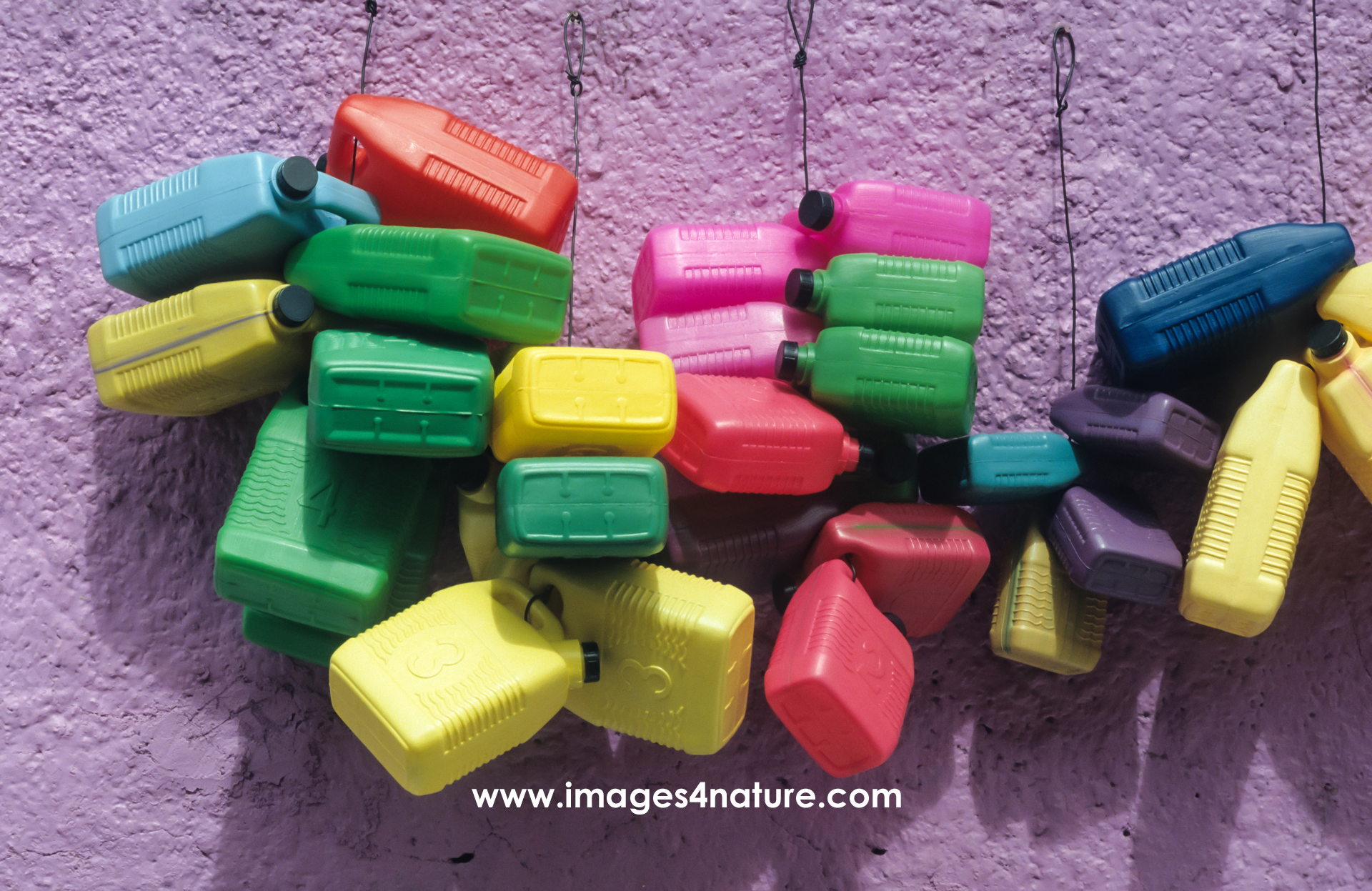 Many plastic containers of different sizes and colors hanging in front of a purple wall