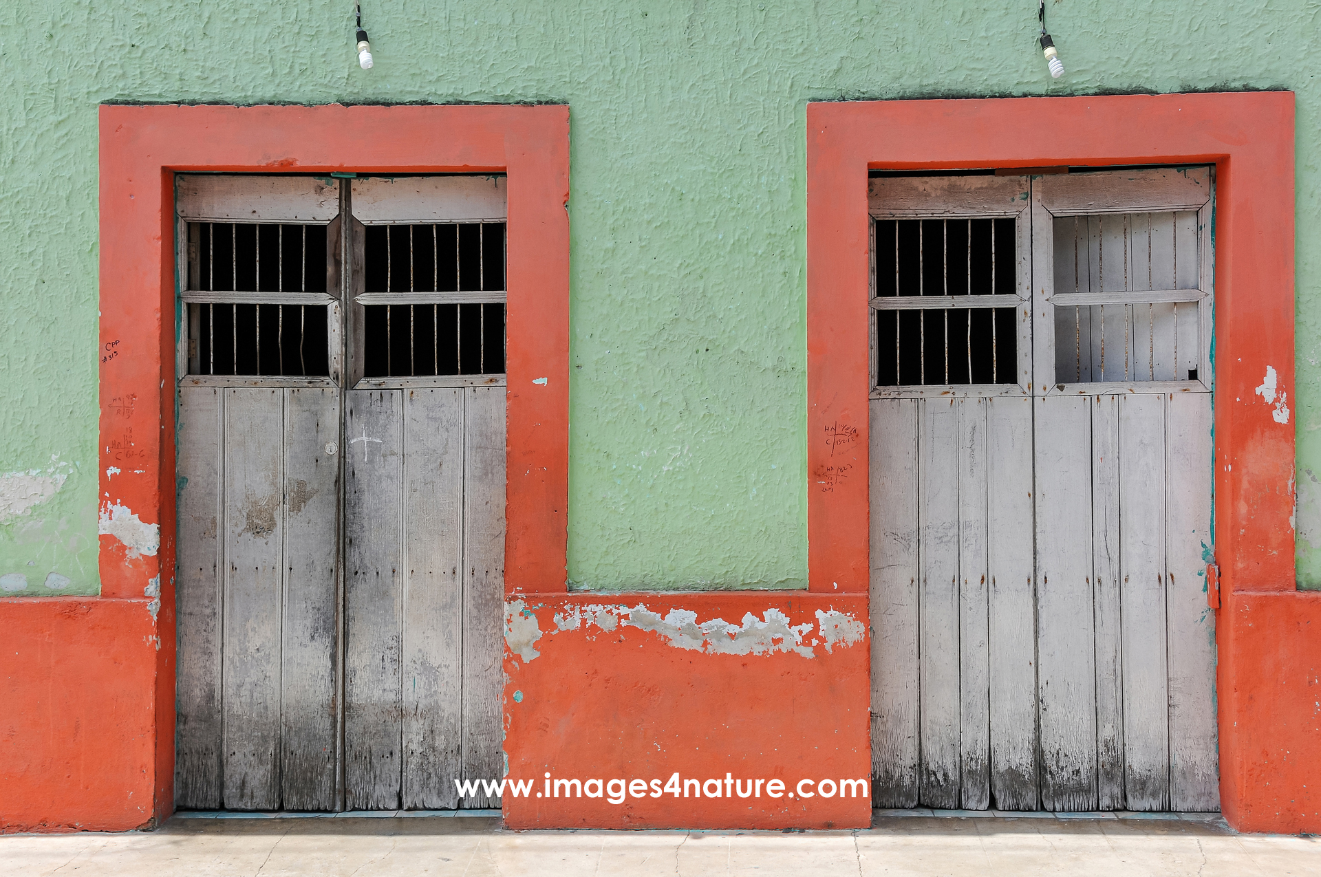 Two identical wooden doors with red frames and an opening in their upper part in a house with green walls