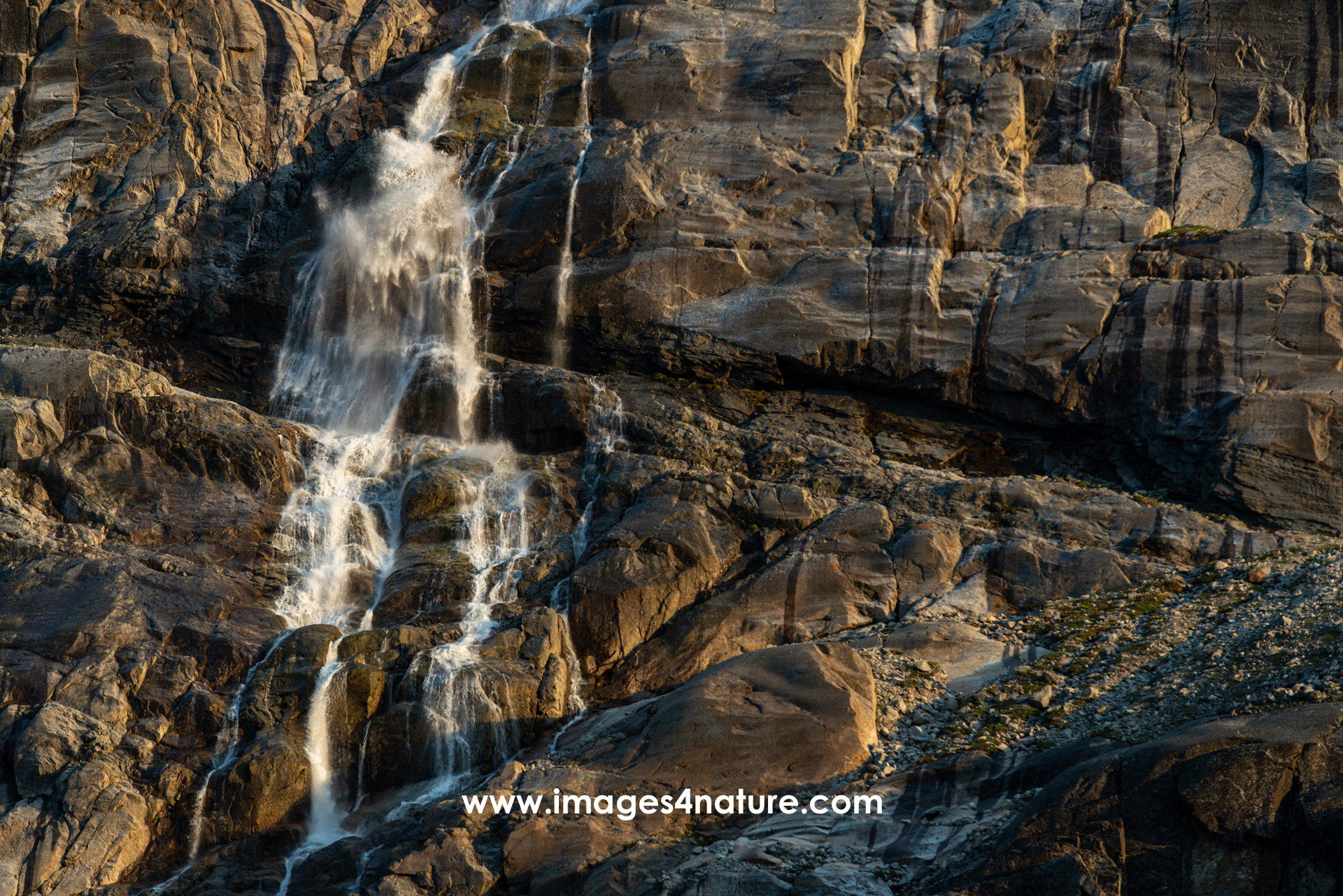 Small waterfall dropping over sun illuminated rocks