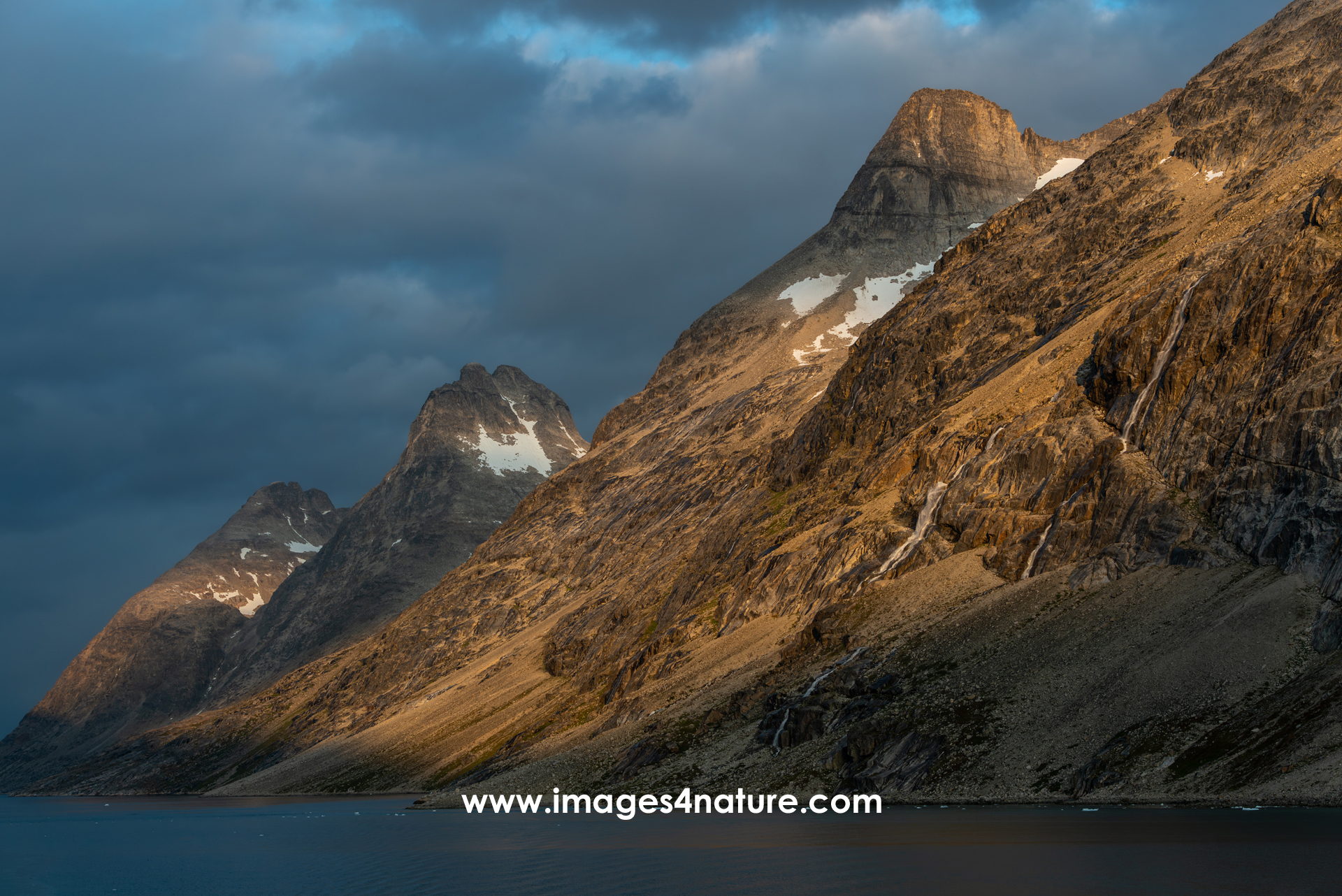 Three mountain peaks lined up behind each other, illuminated by warm evening sunlight