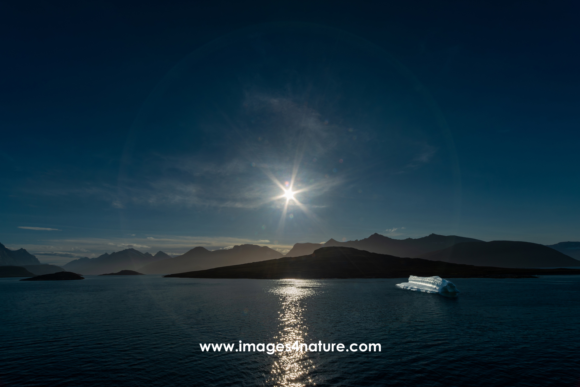 360 degree halo around the sun, shining onto a fjord landscape with a floating iceberg