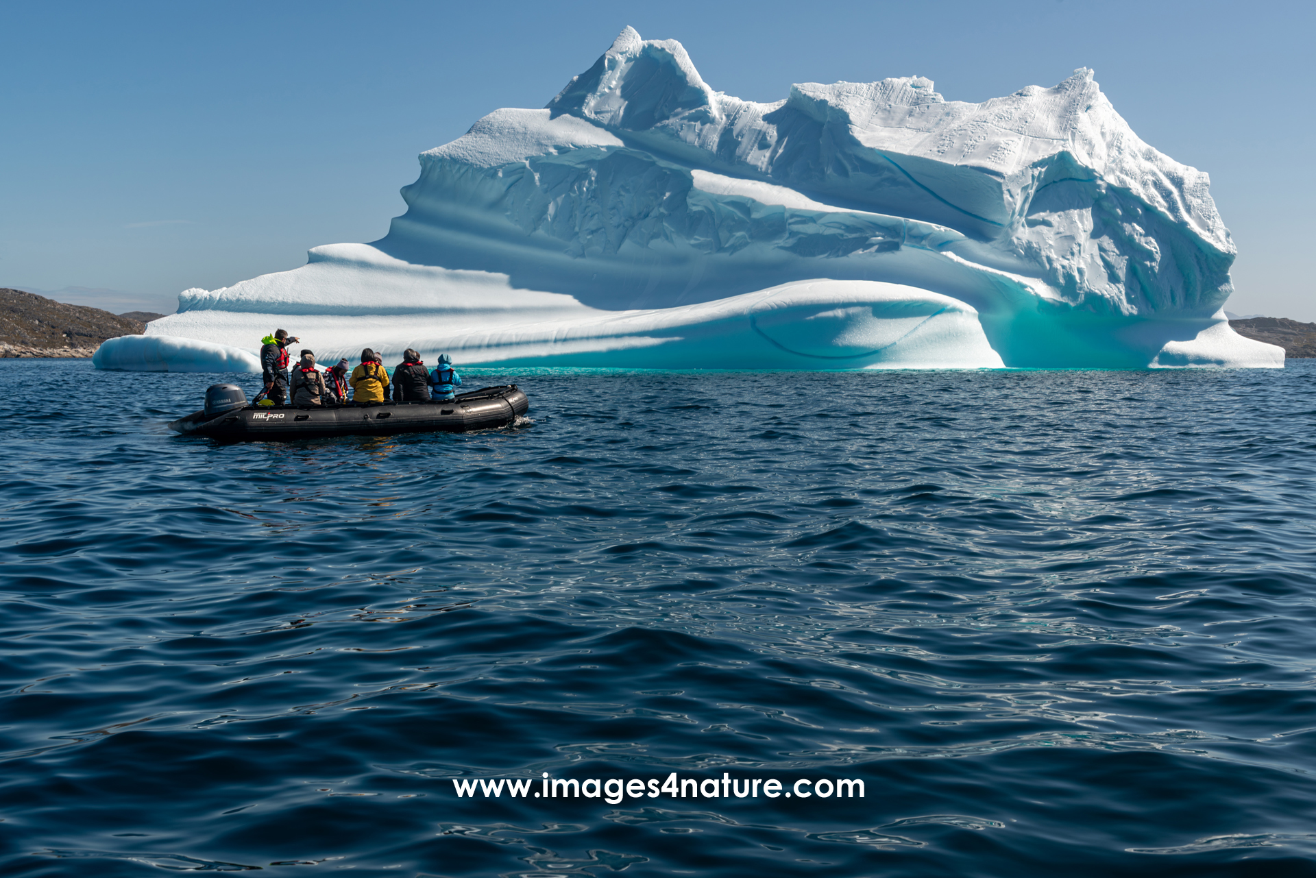 A zodiac with tourists having a closer look at a large iceberg